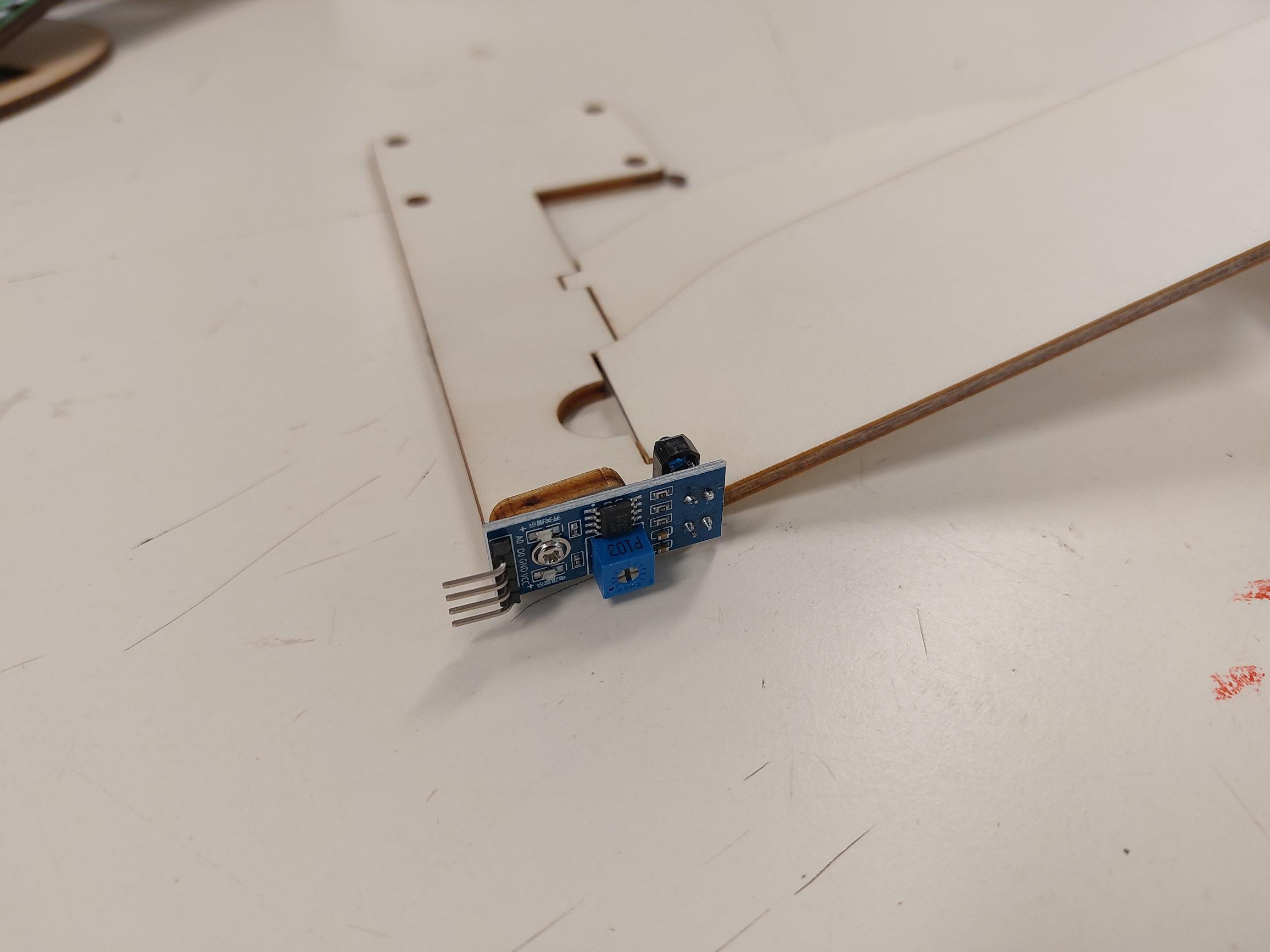 De infraroodsensor met een blauw stelschroefje, vastgezet op de houten baan.